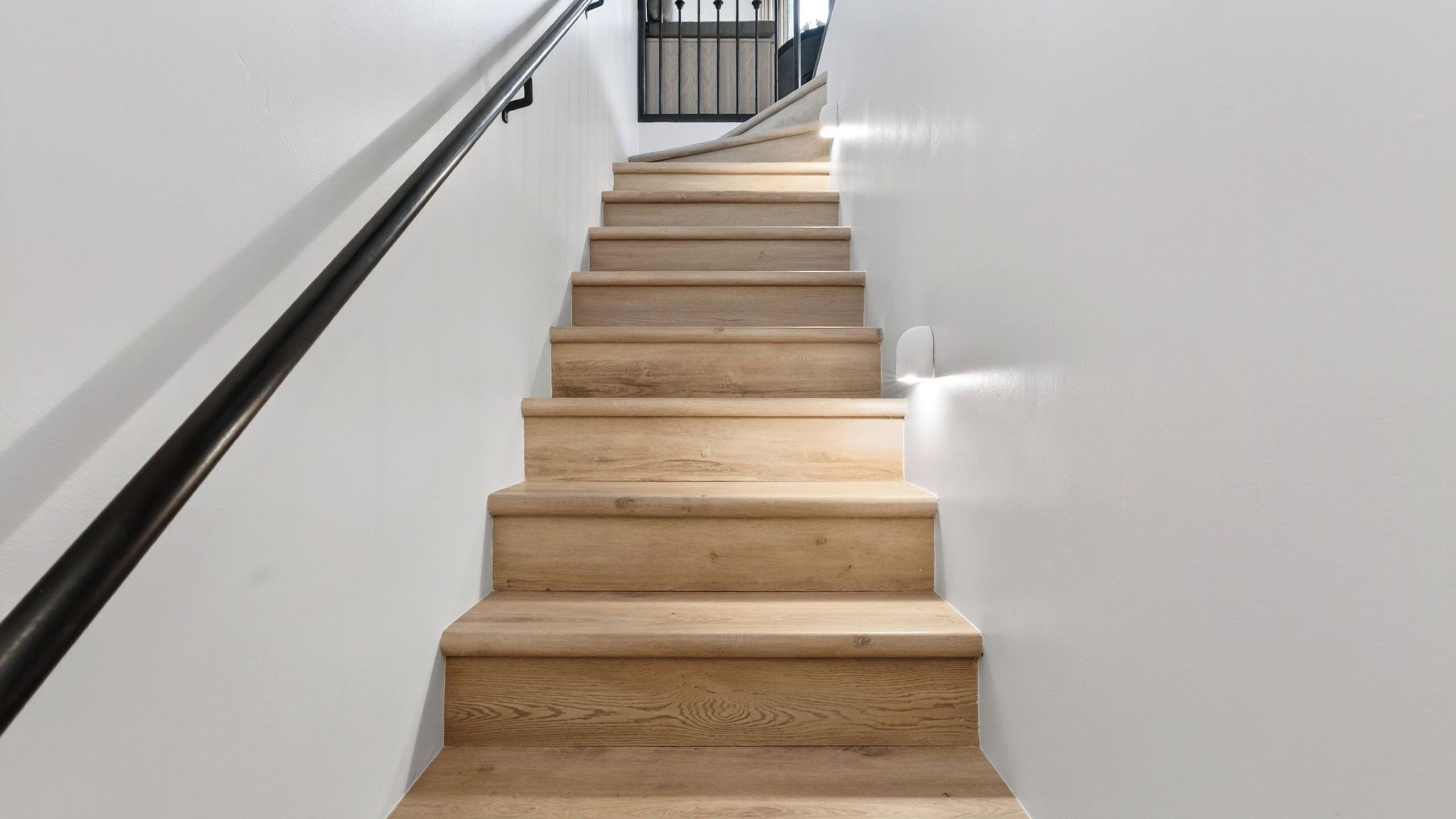 Una escalera de madera con barandilla negra que lleva a una plataforma con baranda metálica.