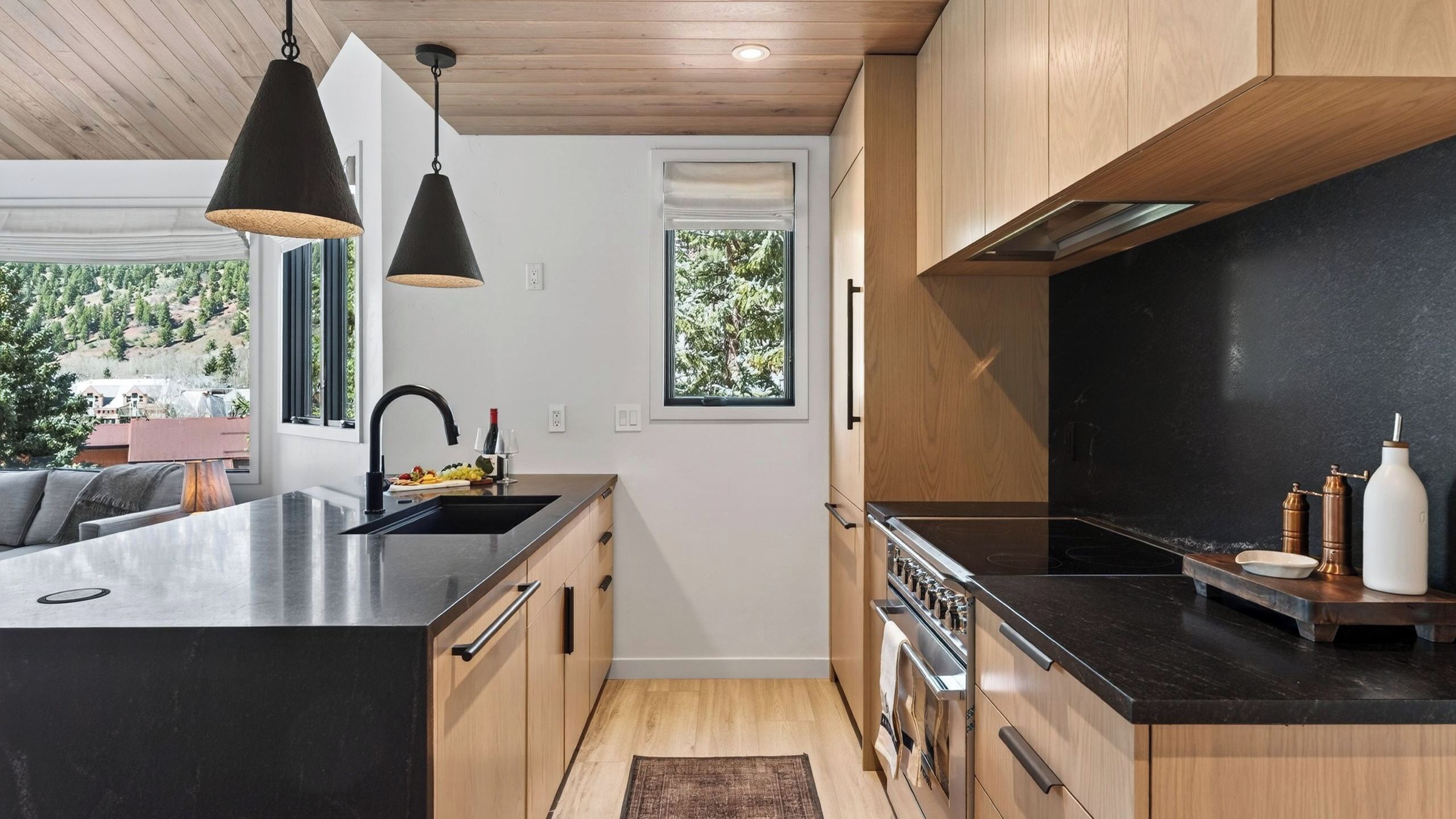Une cuisine moderne dotée d’un îlot central, de meubles en bois, d’un plan de travail noir et de luminaires suspendus.