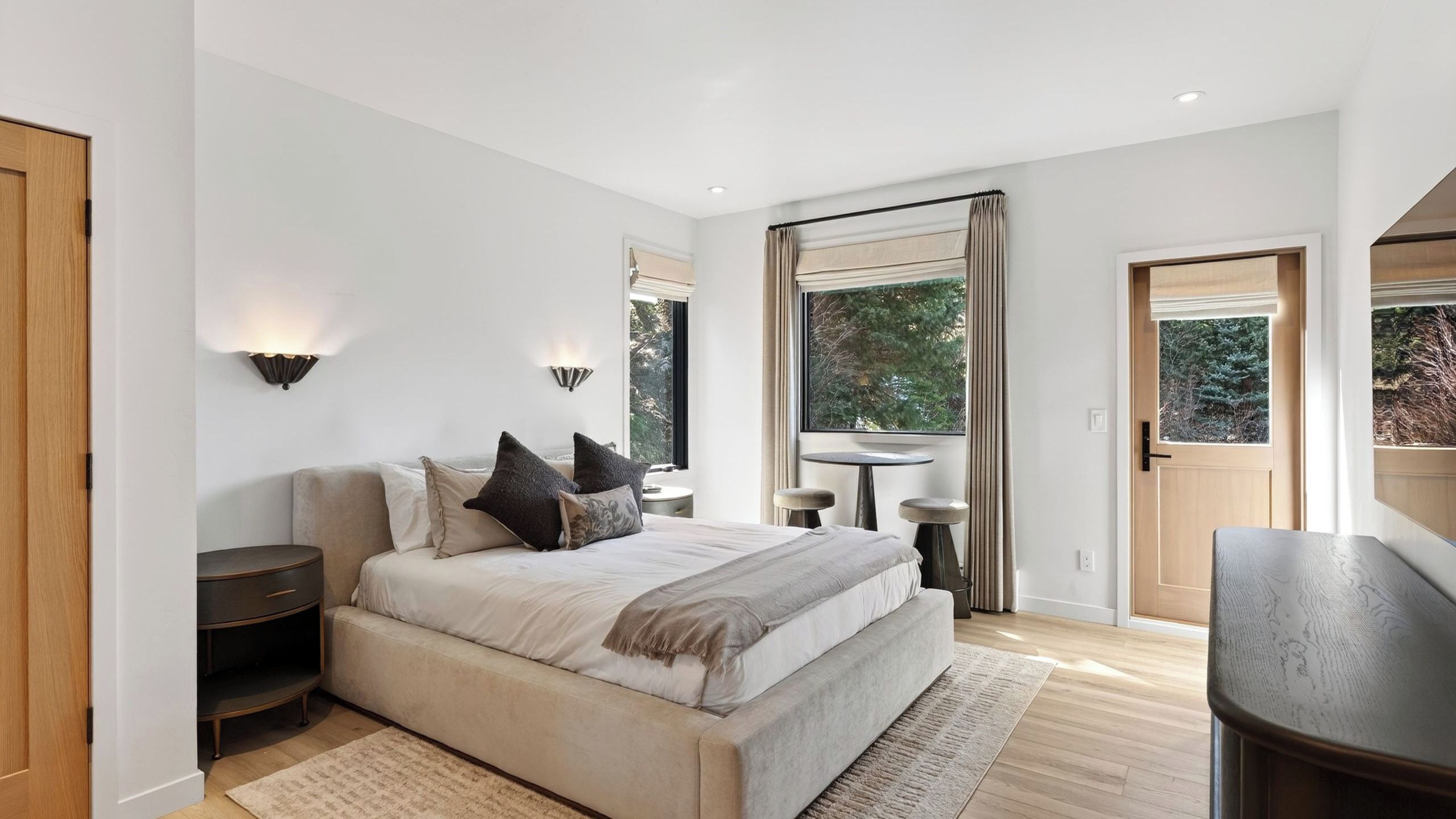 Une chambre à coucher avec un lit, des tables de chevet, un bureau et une grande fenêtre.