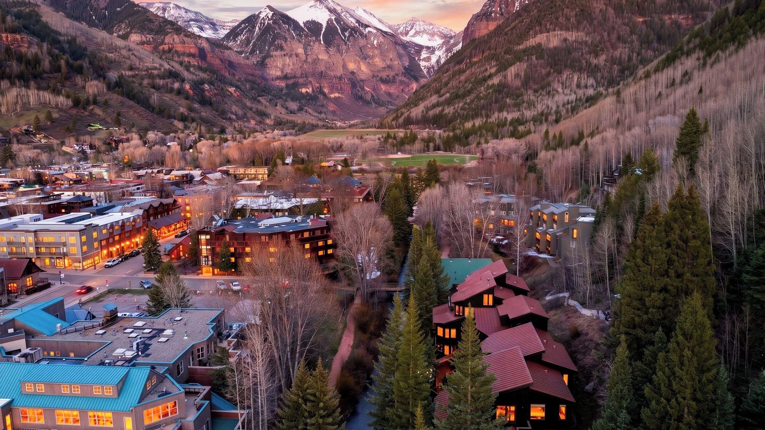 A mountainous town with buildings, a river, and snow-capped peaks in the background.