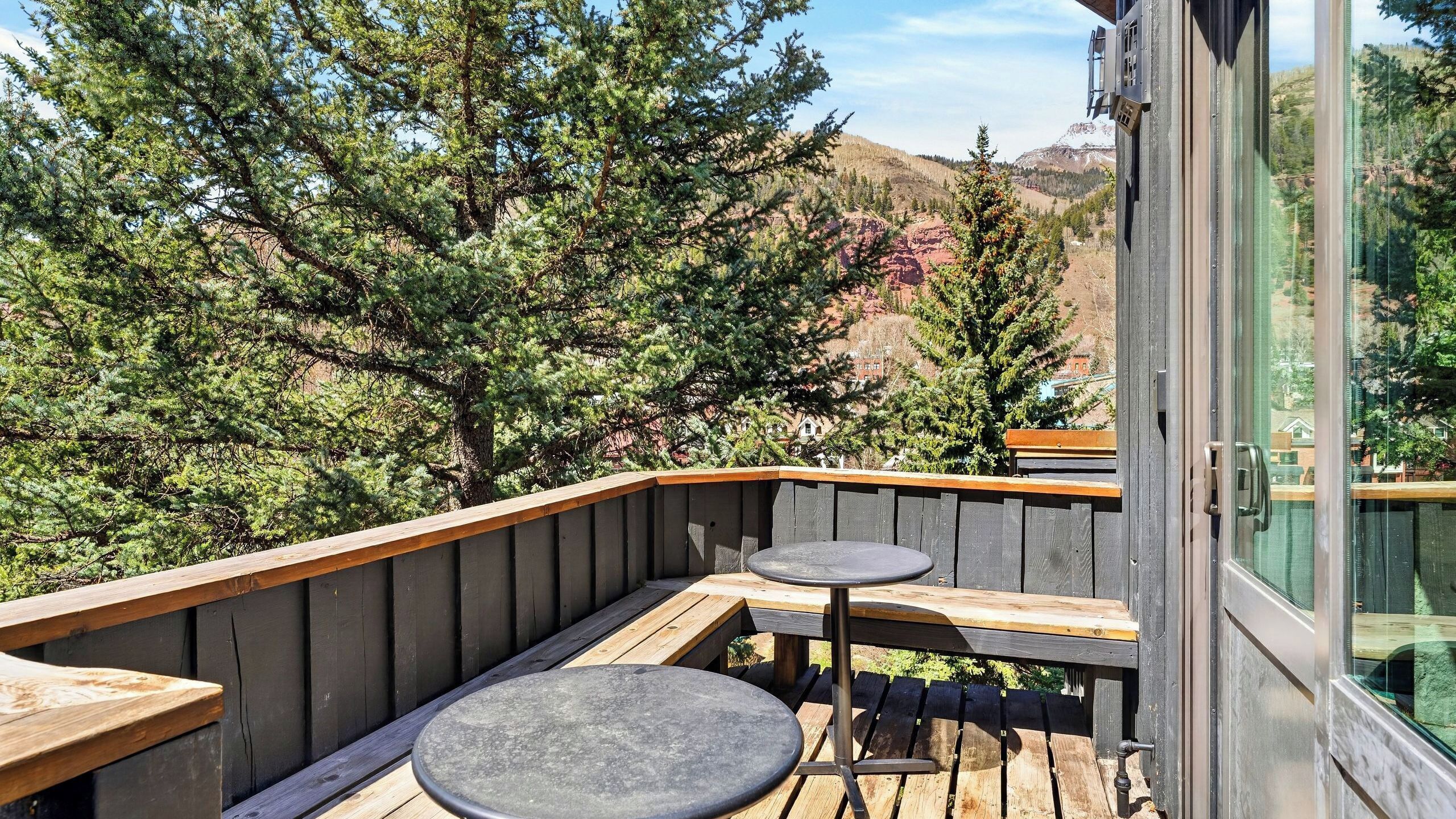 Ein Balkon mit Holzwertkasten, zwei runden Tischen und einer Glastür.