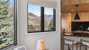 A kitchen with a large window, wooden cabinets, a black faucet, and a dining area with two chairs. - Riverstone Retreat by Avantstay Shared Hot Tub + Mountain Views Walk to Gondola + San Miguel River Trail (Telluride)