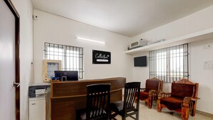 A reception area with a wooden desk, two black chairs, a red sofa, a TV, and a sign that reads 'Collection & Company Services'.