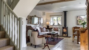 A spacious living room with a fireplace, a sofa, a dining table, and a staircase. - Roundhill Farm Cottage - Naunton, Bourton-on-the-Water, sleeps 4 guests  in 2 bedrooms (Cheltenham)