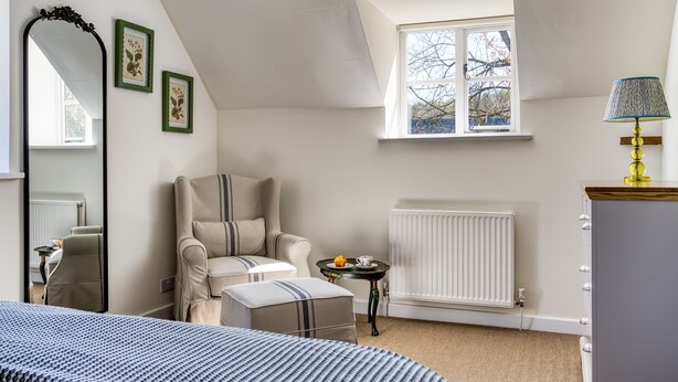 A bedroom with a bed, a chair, a small table, a radiator, and a window with a view. - Roundhill Farm Cottage - Naunton, Bourton-on-the-Water, sleeps 4 guests  in 2 bedrooms (Cheltenham)