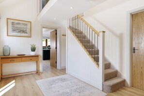A modern interior with a wooden desk, a staircase with a wooden handrail, and a door with a textured panel. - Norton Subedge Barn -  Mickleton, Chipping Campden sleeps 6 guests (Mickleton)