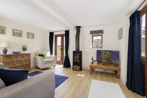 A living room with a sofa, a wooden cabinet, a TV, and a fireplace. - Norton Subedge Barn -  Mickleton, Chipping Campden sleeps 6 guests (Mickleton)