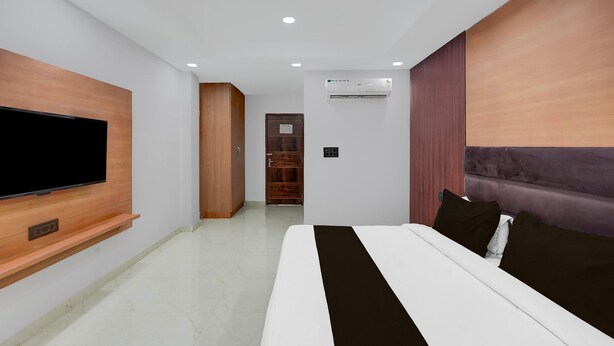 A modern hotel room with a large bed, a flat-screen TV mounted on the wall, a wardrobe, and an air conditioning unit. - Super Collection O Sector 18 Metro Station (Noida)