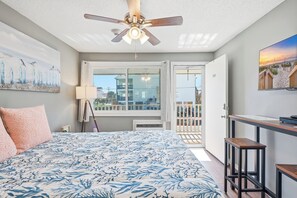 A bedroom with a bed, ceiling fan, artwork, and a balcony with a view. - Paws & Palms-Pet Friendly-Pool-Free Parking (North Myrtle Beach)