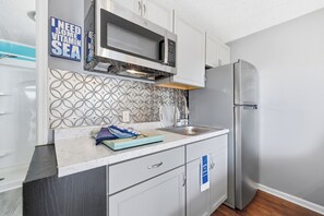 A modern kitchen with a microwave, stainless steel refrigerator, and a decorative backsplash. - Paws & Palms-Pet Friendly-Pool-Free Parking (North Myrtle Beach)