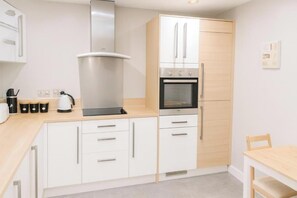 A modern kitchen with white cabinetry, a stainless steel range hood, a built-in oven, and a wooden countertop. - Sleeps 4 - Parking - Wifi (Cardiff)