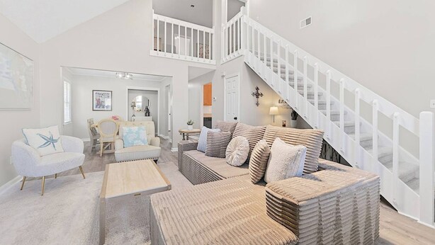 A spacious living room with a high ceiling, a white staircase, and a view of the upper floor. - Newly Renovated VB Retreat Comfort Space Home (Virginia Beach)