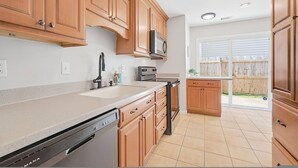 A kitchen with wooden cabinets, a dishwasher, a microwave, and a window with a view of a wooden fence. - Newly Renovated VB Retreat Comfort Space Home (Virginia Beach)