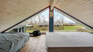A bedroom with a sloped ceiling, a bed, a chair, and a window overlooking a yard.