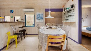 A wooden interior with a dining table set for four, a kitchen area, and a bed.