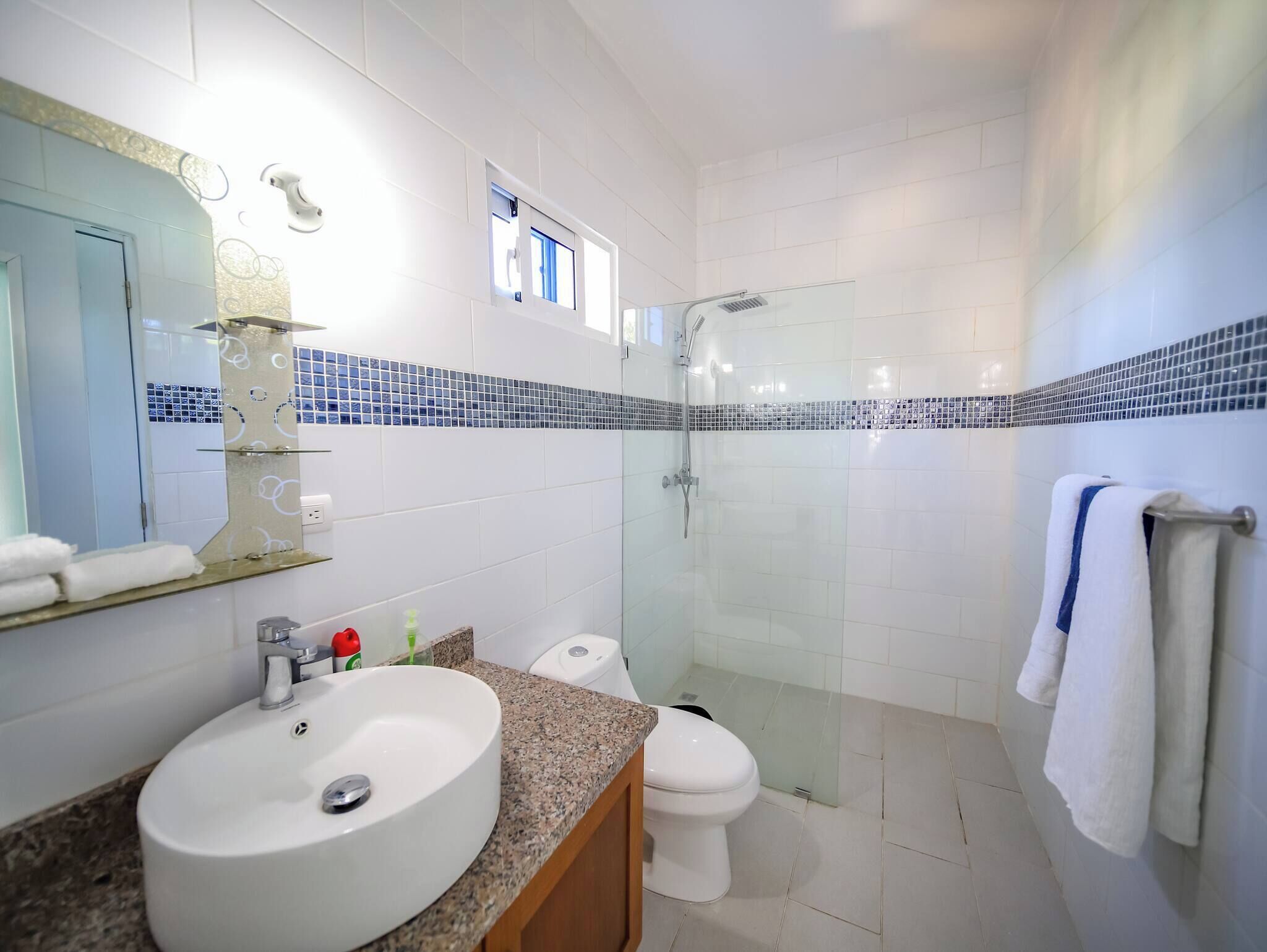 A modern bathroom with a large mirror, a sink, a toilet, and a glass-enclosed shower.
