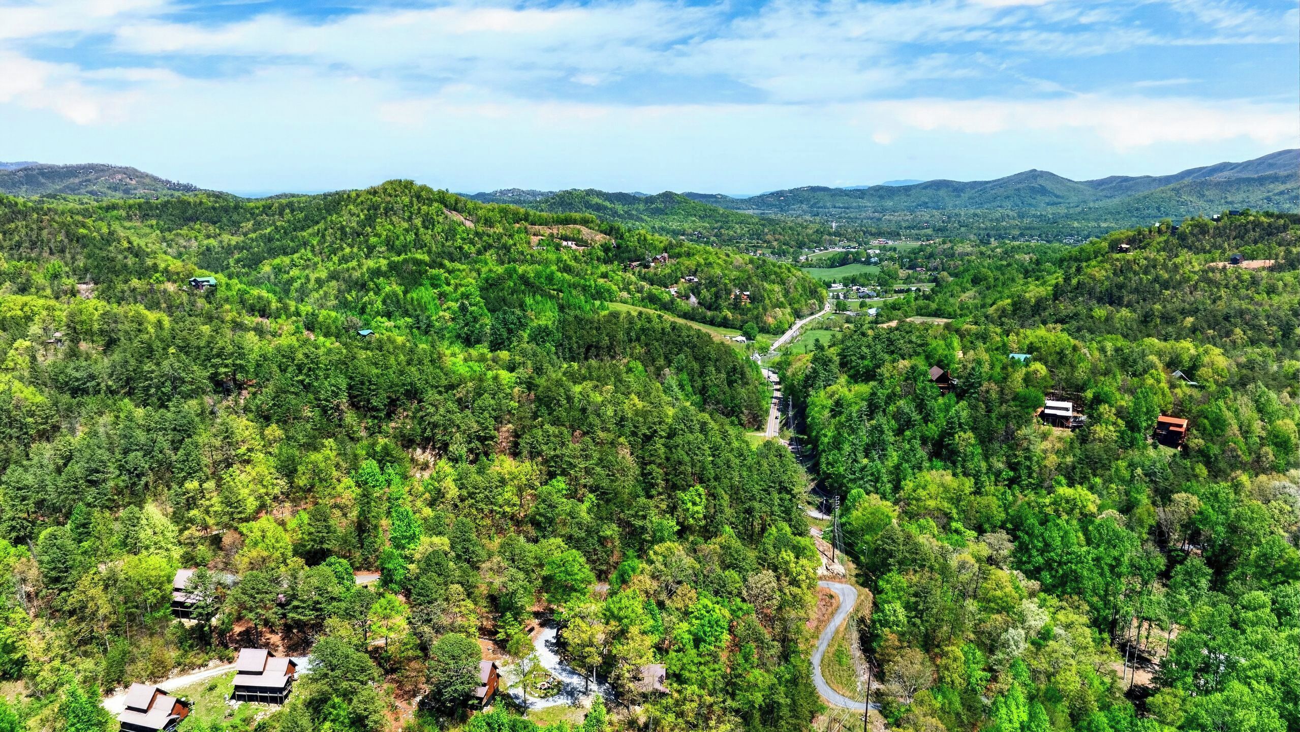Une vallée boisée, traversée par une route sinueuse et parsemée de bâtiments.
