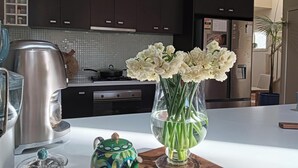 Eine Küche mit dunklen Schränken, einem Edelstahl-Wasserkocher, einer klaren Vase mit weißen Blumen und einem bunten Teekessel.