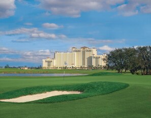 Un parcours de golf avec un bunker de sable, un mât de drapeau et, au loin, un grand bâtiment d’hôtel.