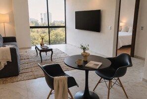 Ein modernes Wohnzimmer mit einer Couch, einem Couchtisch, zwei Sesseln, einem Fernseher und Blick auf die Stadt.