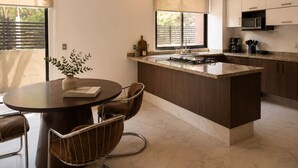 A modern kitchen with a central island, a dining area with a round table and chairs, and a view of the outdoors through large windows. - 3BR · Country Club Guadalajara · cocina · rooftop bar · WiFi (guadalajara)