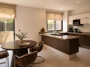 A modern kitchen with a central island, a dining area with a round table and chairs, and a view of the outdoors through large windows. - 3BR · Country Club Guadalajara · cocina · rooftop bar · WiFi (guadalajara)