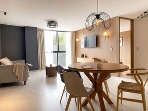 A modern living room with a sofa, dining table, chairs, and a TV. - Japandi en Country Club GDL · caminable · rooftop · limpieza diaria (guadalajara)