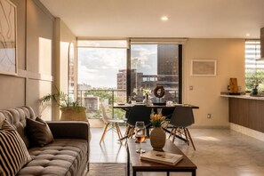 Een moderne woonkamer met een bank, een eettafel met stoelen, een salontafel en een groot raam met uitzicht op de stad.