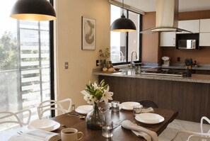 A modern kitchen with a dining area, featuring a large window, pendant lights, and a view of the outdoors. - Suite vintage · rooftop bar · Country Club GDL · limpieza diaria (guadalajara)