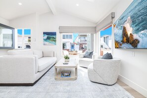 Ein modernes Wohnzimmer mit Sofa, Sessel, Couchtisch und einem Gemälde mit Küstenlandschaft.