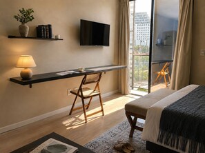 Ein modernes Hotelzimmer mit Schreibtisch, Stuhl, Bett, Fernseher und einem Balkon mit Sitzgelegenheit.