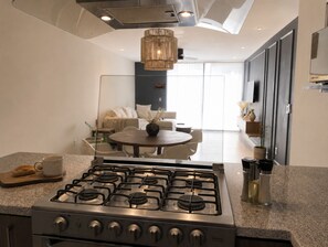 A modern kitchen with a gas stove, a dining area with a round table, and a living room with a sofa. - Rooftop bar + vistas altas · Country Club GDL · limpieza diaria (guadalajara)