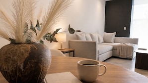 Ein modernes Wohnzimmer mit einer Couch, einem Couchtisch, einer Vase mit Trockenpflanzen, einer Lampe und einem Notizbuch.
