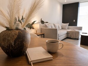A modern living room with a sofa, a coffee table, a vase with dried plants, a lamp, and a notebook. - Rooftop bar + vistas altas · Country Club GDL · limpieza diaria (guadalajara)