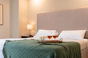 A neatly made bed with a green blanket, two glasses of amber liquid, and a tray with flowers on a hotel room. - Estudio Premier · vistas · Country Club GDL · limpieza diaria (guadalajara)