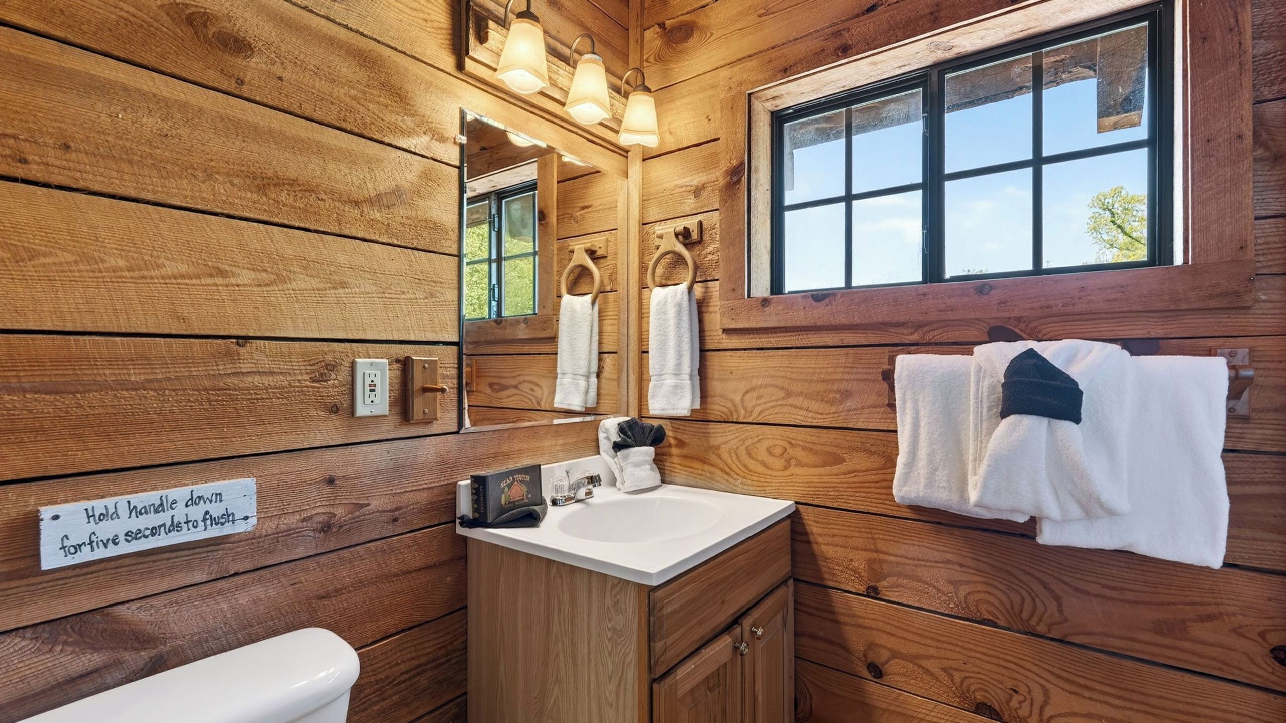 Een houten badkamer met een toilet, wastafel en handdoekhouder.