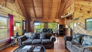 A wooden cabin interior with a sofa, a coffee table, and a dining area. - Anna's Cabin by Avantstay Private Hot Tub + Mountain Views + Covered Deck 7 Min to Townsend (Townsend)