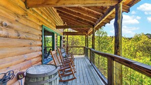 A wooden cabin with a porch, rocking chairs, and a barrel.