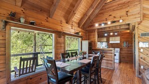 A wooden cabin with a dining area, kitchen, and large windows. - Anna's Cabin by Avantstay Private Hot Tub + Mountain Views + Covered Deck 7 Min to Townsend (Townsend)