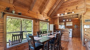 A wooden cabin with a dining area, kitchen, and large windows.