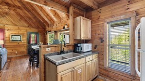 A wooden cabin interior with a kitchen area, dining table, and chairs. - Anna's Cabin by Avantstay Private Hot Tub + Mountain Views + Covered Deck 7 Min to Townsend (Townsend)