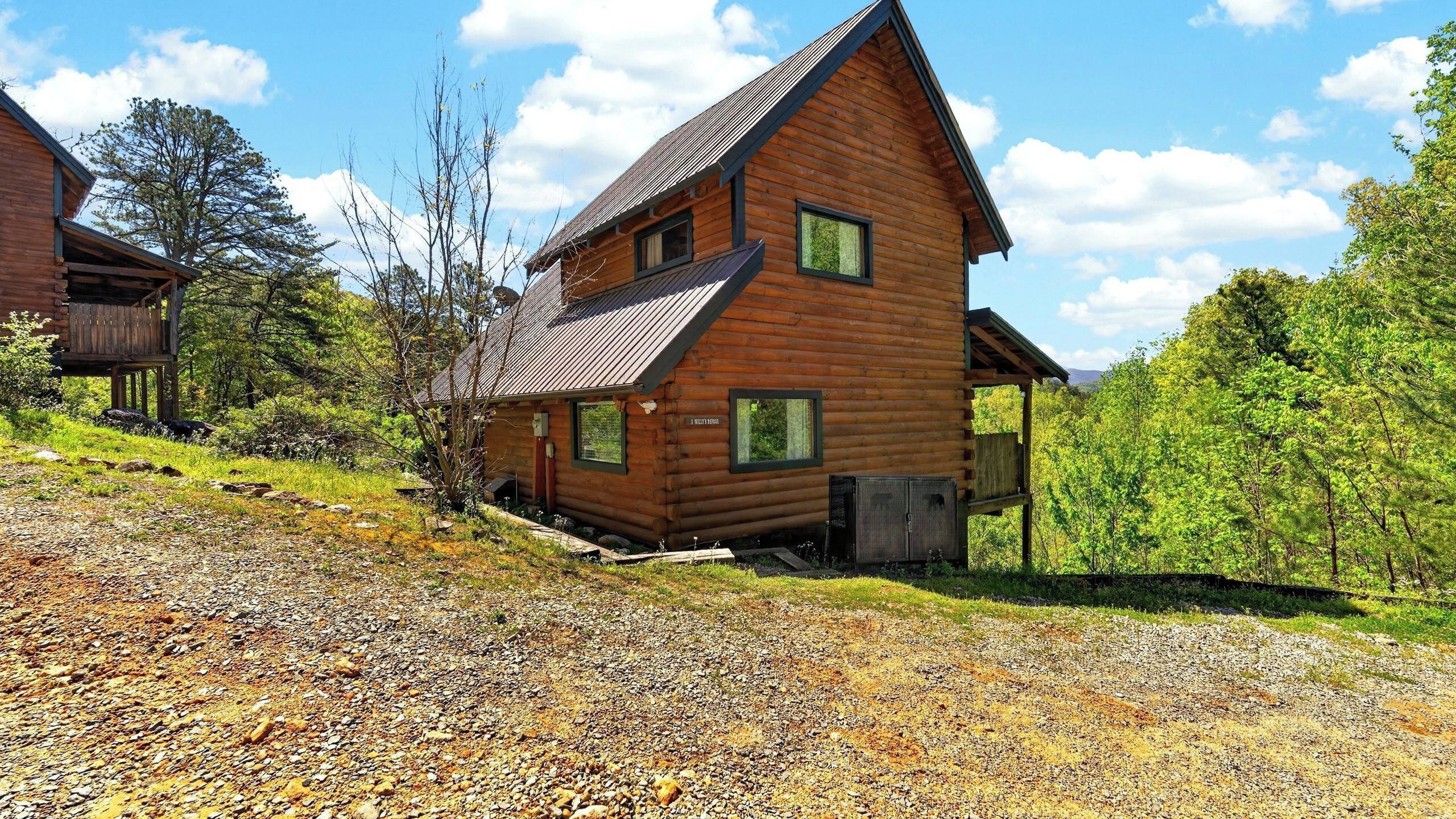 Une cabane en rondins avec un toit en pente, une terrasse en bois et une allée gravillonnée.