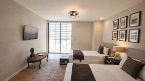 A hotel room with two beds, a desk, a TV, and a large window with blinds. - Junior suite · vistas + rooftop · Country Club · limpieza diaria (guadalajara)