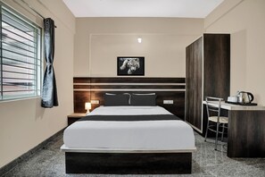 Ein Hotelzimmer mit einem Bett, einem Schreibtisch mit Stuhl, einem Bild an der Wand und einem Fenster mit Jalousien.