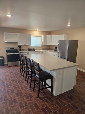 A kitchen with a central island, bar stools, a refrigerator, and a microwave. - 4 King beds, 3 bunk beds, perfect family getaway close to downtown Cody. (Cody)