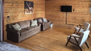 Un salon avec un mur en bois, un grand canapé, deux fauteuils, un téléviseur à écran plat et un tapis.