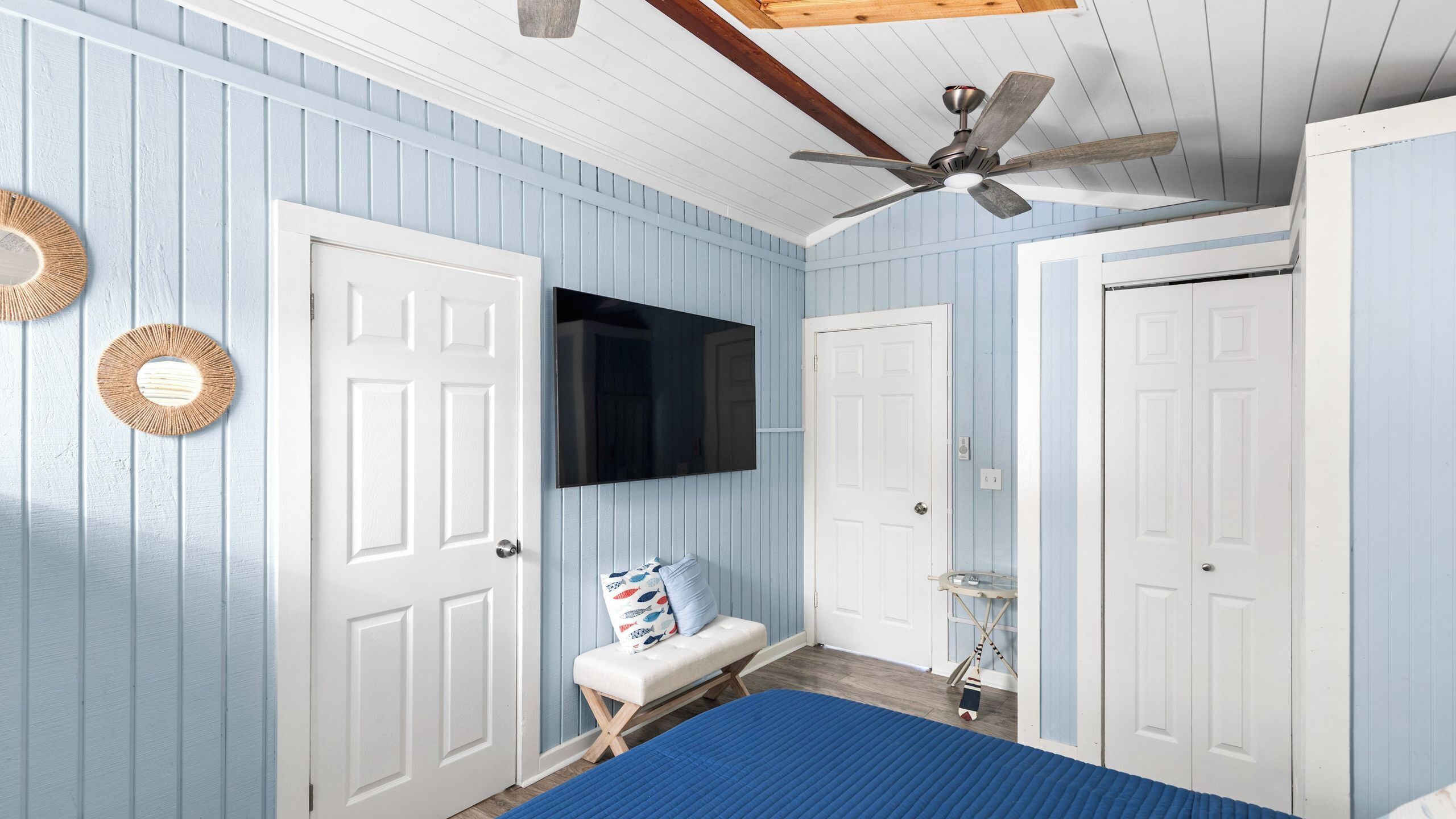 Un dormitorio con cama, ventilador de techo, televisión y dos puertas.
