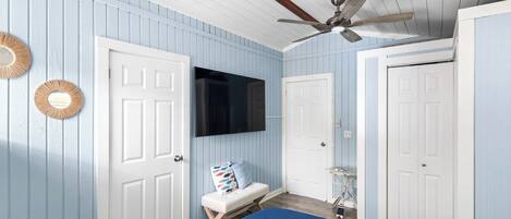 Un dormitorio con cama, ventilador de techo, televisión y dos puertas.