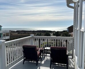 A balcony with two chairs and a table, overlooking a beach and ocean. - Bee by the Sea, 5 BR house 1 minute to the beach, private road near restaurants (Oak Island)