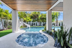 Een ruimte met een hottub, een houten pergola, een kleine glijbaan en een zwembad op de achtergrond.